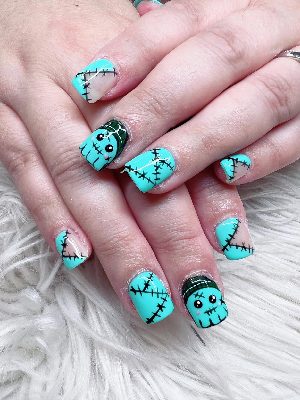 Short square turquoise nails with cute stitched monster faces and black patchwork seam details.