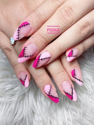 Long matte pink almond nails show black stitched lines crossing hot-pink corner blocks in a patchwork pattern.