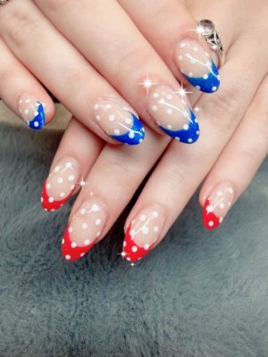 Almond nails with red and blue French tips and white polka dots on a sheer base.