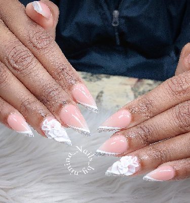 Long pink almond nails with thin white diagonal French tips, silver glitter edges, and raised white flower accents on both hands.