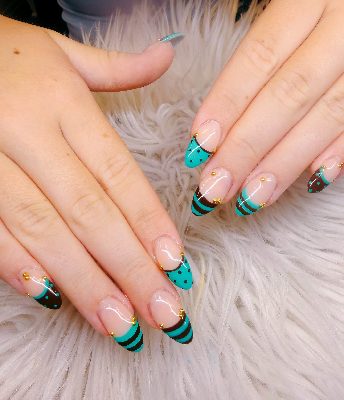Long almond nails with nude-pink bases, turquoise and dark-brown striped French tips, polka dots, curved sections, and small gold studs.
