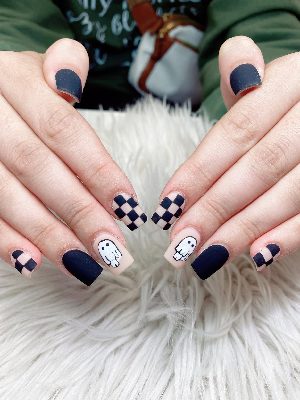 Short square nails with matte black and nude-pink polish, black checkerboard patterns, and simple white ghost accents.