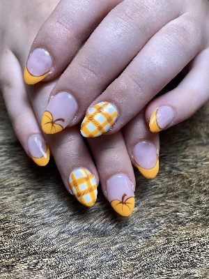 Medium almond nails with orange French tips, pumpkins, and orange-and-white plaid accents on a pink base.