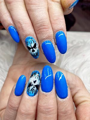 Long almond nails in bright glossy blue with two accent nails featuring black and white skull faces and dark streaks.