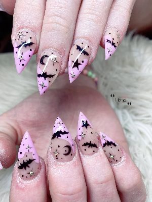 Extra-long pink stiletto nails with black bats, moons, stars, dots, dripping accents, and small rhinestones.