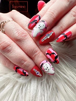 Long pink and red stiletto nails with white cartoon-inspired ghosts, black bats and stars, plus crystal accent clusters.