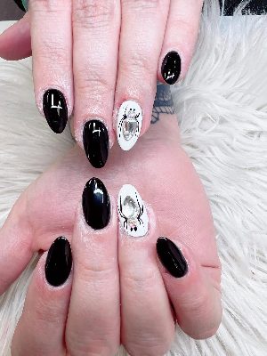 Glossy black almond nails alternate with white spider accent nails featuring large clear rhinestones.