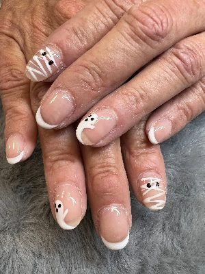 Short round nude nails with white French tips, small ghosts and white mummy-wrap accents with black eyes.