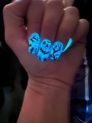 A dimly lit hand shows blue glowing coffin nails with black horror-face artwork.