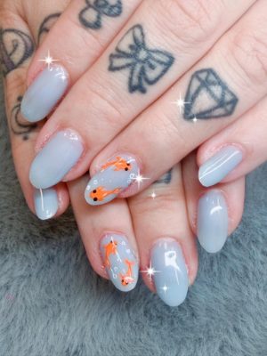 Pale gray oval nails with orange fish accent art and small bubble dots.