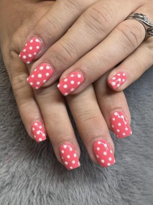 Square coral pink nails covered with evenly spaced white polka dots.