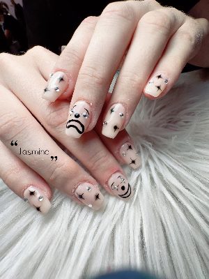 Medium square pink nails with black sad faces, starbursts, and scattered silver rhinestones.