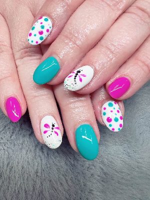 Medium oval nails in teal, pink, and white with colorful polka dots, dragonfly motifs, and small silver glitter accents.