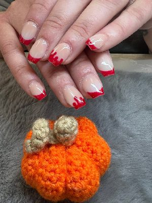 Medium square nails with a glossy nude base, red French tips and red dripping details on accent nails.