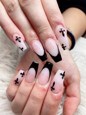 Long pink coffin nails have glossy black deep French tips and scattered black cross silhouettes.