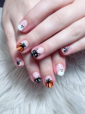 Short round nude-pink nails with orange pumpkins, white ghosts, black cat faces, and small black spiders.