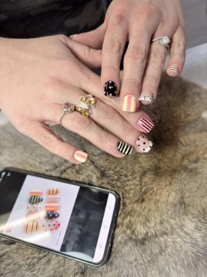 Short nails with mixed stripe and dot designs in pink, yellow, black, white, and nude tones.