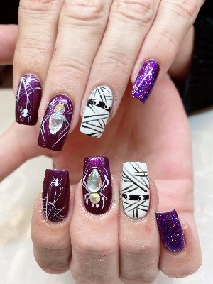 Long purple coffin nails feature white spiders and webs, mummy accents, glitter and large clear rhinestones.