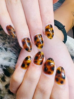 Medium oval nails covered in a glossy tortoiseshell pattern with translucent amber-brown areas and irregular dark brown and black spots.
