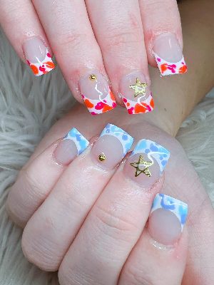 Medium square nails with mismatched blue and orange-pink patterned French tips, white wavy lines, gold studs, and star charms.