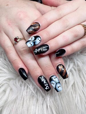 Long black coffin nails with pale blue ghosts, white lettering, and smoky orange and copper glitter accent nails.