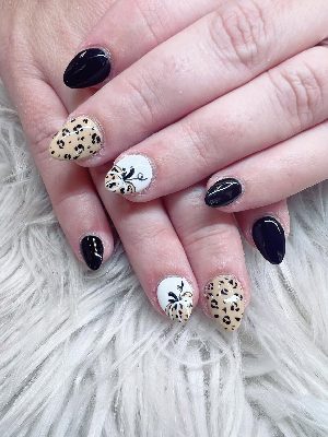 Short almond nails mixing glossy black polish, beige leopard print, and white nails with leopard-patterned pumpkins and vines.