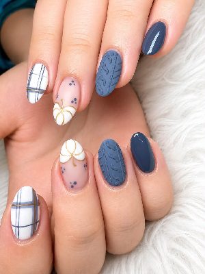 Medium oval nails in navy, slate blue, white, and sheer pink with white pumpkins, gold outlines, plaid lines, dots, and raised cable-knit texture.