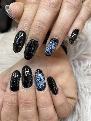 Long almond nails with glossy black glitter polish and pale blue spiral galaxy accents.