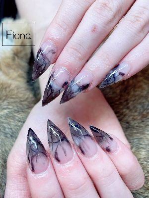 Extra-long stiletto nails with translucent pink bases and smoky black-gray marble concentrated toward the pointed tips.