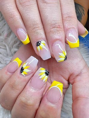 Long glossy coffin nails with a sheer pink base, bright yellow French tips, and white-and-yellow sunflower artwork with black centers.