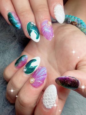 Almond nails with teal shimmer waves, pink shell accents, white scale patterns, and raised gem details.