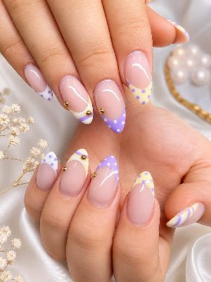 Long almond nails with nude-pink bases and mismatched purple, yellow, and white French tips featuring dots, stripes, and gold studs.