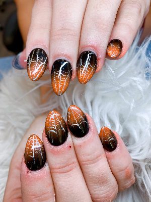 Medium almond nails with glossy orange-to-black gradients and fine silver spiderweb patterns.
