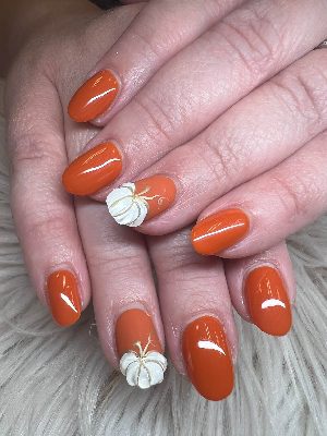 Glossy medium oval orange nails with raised white pumpkin accent art and fine gold stems and vines.