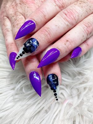 Extra-long purple stiletto nails with raised dark skull accents, black rhinestones, and silver glitter tips.